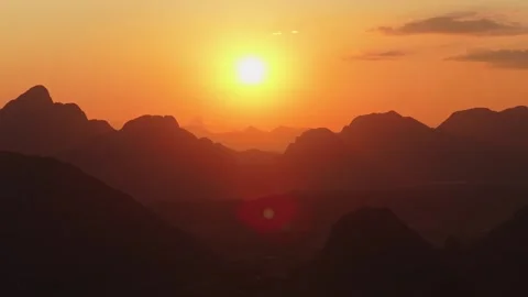 Paramotor flies over silhouetted mountains in Vang Vieng, Laos during a warm sun Vídeos de archivo 335311477