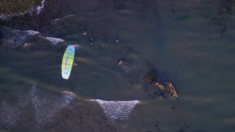 Paramotor flying over a shipwreck with waves washing over wreck. Stock Footage 142064078