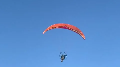 A paramotor pilot soaring high in the blue sky with an orange paraglider Stock Footage 292286408