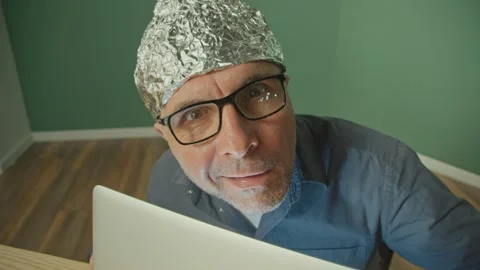 A Paranoid Man in a Protective Foil Cap Working on a Laptop Anxiously Peering Up Video stock 166653859