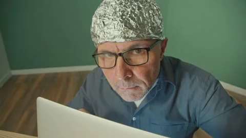 A Paranoid Man in a Protective Foil Cap Working on a Laptop Anxiously Peering Up Stock Footage 166705823