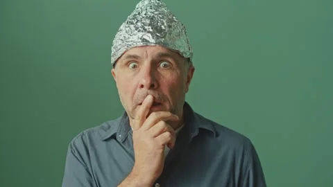 A Paranoid Man with a Protective Foil Cap on his Head Looks Around Anxiously Video stock 166706347