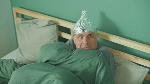 A Paranoid Man with a Protective Foil Cap On His Head, Lying in Bed. Stock Footage 166707936