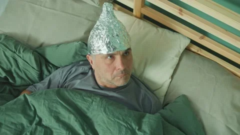 A Paranoid Man with a Protective Foil Cap On His Head, Lying in Bed. Stock Footage 166707959