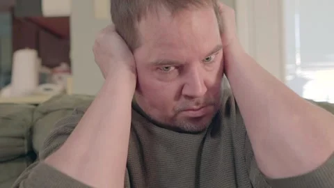 Paranoid man with sitting on couch grabs his ears hearing voices. Video stock 169734385