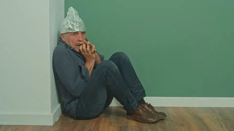 A Paranoid Sitting in a Corner with a Protective Foil Cap on His Head Stock Footage 166650159