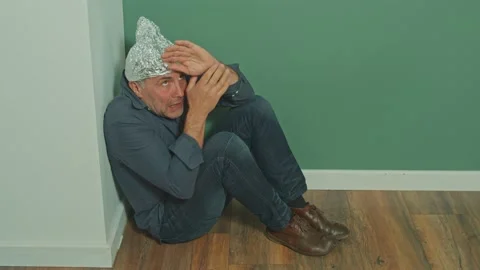 A Paranoid Sitting in a Corner with a Protective Foil Cap on His Head Stock Footage 166652112
