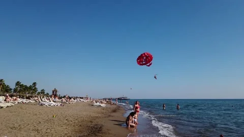 Parasailing on the beach. Two tourists under the canopy of a red parachute. Video stock 198416449