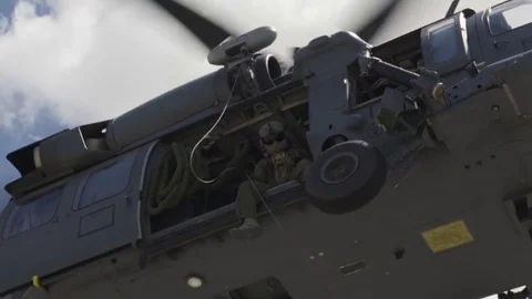Parasrescueman sitting at side of Black Hawk helicopter while hovering Stock Footage 85302925