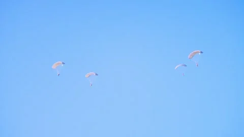Paratroopers float down with open parachutes against a clear blue sky, Video stock 286295074