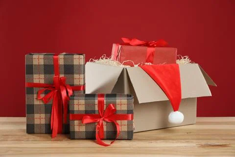 Parcel with gift boxes and Santa hat on wooden table against red background Foto stock