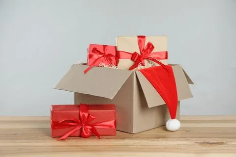 Parcel with gift boxes and Santa hat on wooden table against light background 스톡 사진
