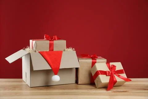 Parcel with gift boxes and Santa hat on wooden table against red background Foto stock