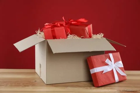 Parcel with gift boxes on wooden table against red background Foto stock