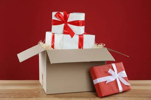 Parcel with gift boxes on wooden table against red background 스톡 사진