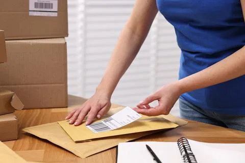 Parcel packing. Post office worker sticking barcode on bag at wooden table .. Photos