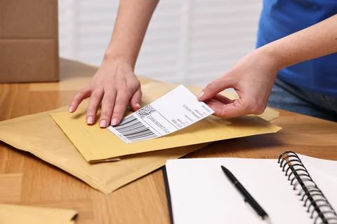 Parcel packing. Post office worker sticking barcode on bag at wooden table .. Photos