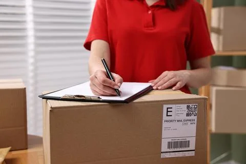 Parcel packing. Post office worker with clipboard and box indoors, closeup Foto stock
