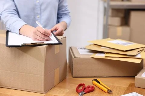 Parcel packing. Post office worker with clipboard writing notes at wooden t.. Foto stock