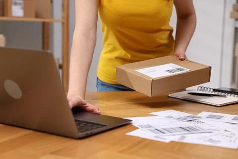 Parcel packing. Post office worker with box using laptop at wooden table in.. Stock Photos