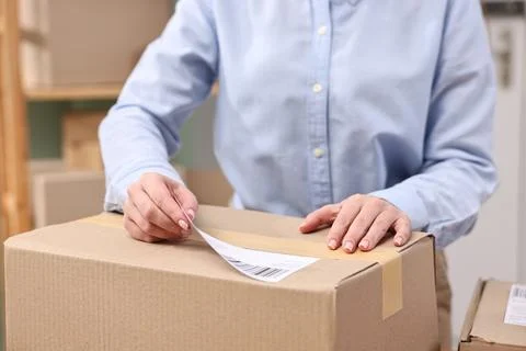 Parcel packing. Post office worker sticking barcode on box indoors, closeup Photos