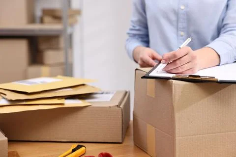 Parcel packing. Post office worker with clipboard writing notes at wooden t.. Stock Photos