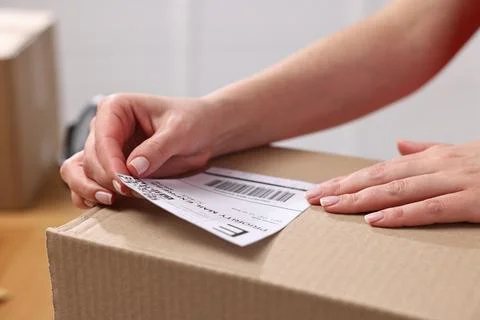 Parcel packing. Post office worker sticking barcode on box indoors, closeup Photos