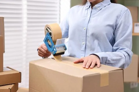 Parcel packing. Post office worker taping box indoors, closeup Photos
