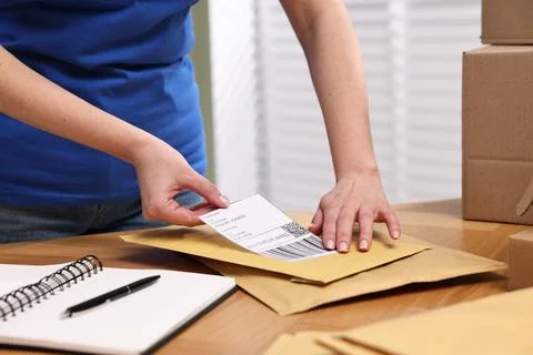 Parcel packing. Post office worker sticking barcode on bag at wooden table .. Photos