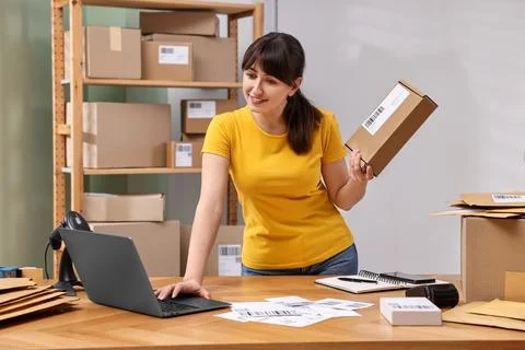 Parcel packing. Post office worker with box using laptop at wooden table in.. Photos