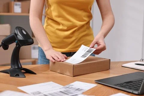 Parcel packing. Post office worker sticking barcode on box at wooden table .. Stock Photos