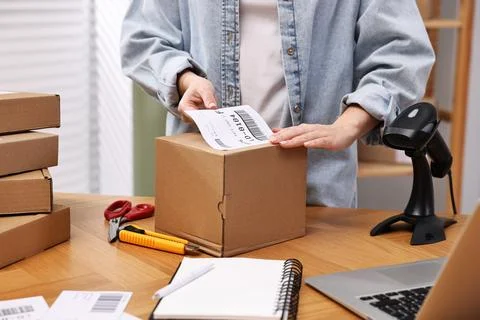 Parcel packing. Post office worker sticking barcode on box at wooden table .. Stockfoto's