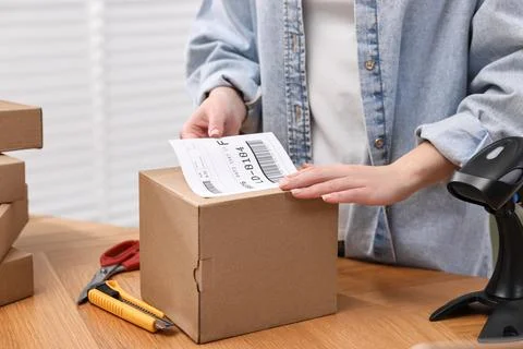 Parcel packing. Post office worker sticking barcode on box at wooden table .. Photos