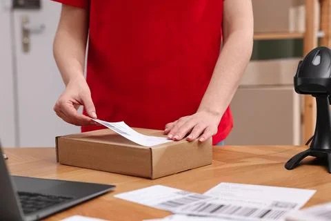 Parcel packing. Post office worker sticking barcode on box at wooden table .. Photos