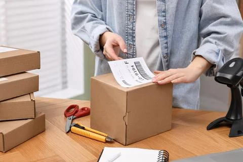 Parcel packing. Post office worker sticking barcode on box at wooden table .. Foto stock