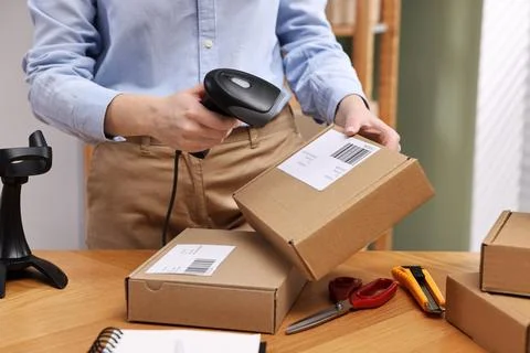 Parcel packing. Post office worker with scanner reading barcode at wooden t.. Stockfoto's