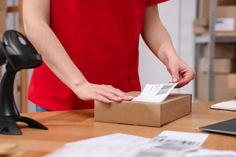 Parcel packing. Post office worker sticking barcode on box at wooden table .. Stock Photos