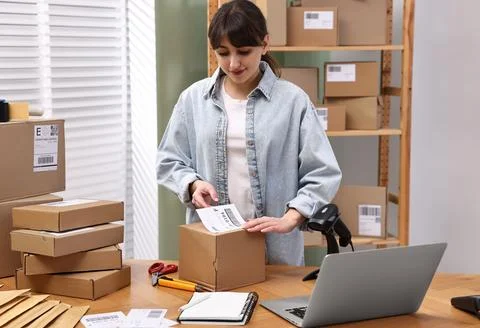 Parcel packing. Post office worker sticking barcode on box at wooden table .. Foto stock