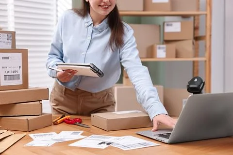 Parcel packing. Post office worker with notebook using laptop at wooden tab.. Foto stock