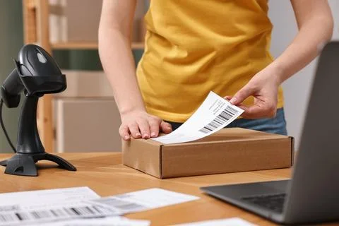 Parcel packing. Post office worker sticking barcode on box at wooden table .. Photos