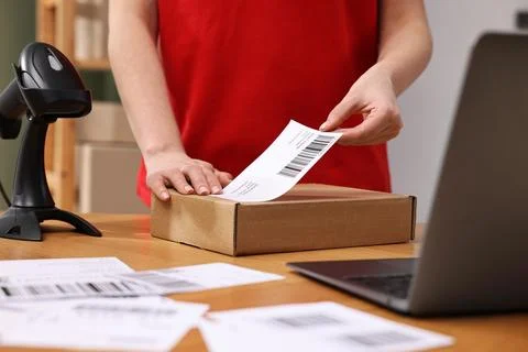 Parcel packing. Post office worker sticking barcode on box at wooden table .. Photos