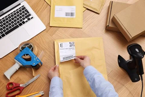 Parcel packing. Post office worker sticking barcode on bag at wooden table,.. Stock Photos
