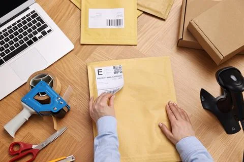 Parcel packing. Post office worker sticking barcode on bag at wooden table,.. Stock Photos