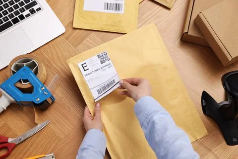 Parcel packing. Post office worker sticking barcode on bag at wooden table,.. Photos