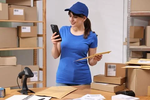 Parcel packing. Post office worker with smartphone and bag indoors Foto stock