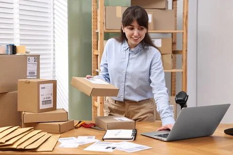 Parcel packing. Post office worker using laptop at wooden table indoors Photos