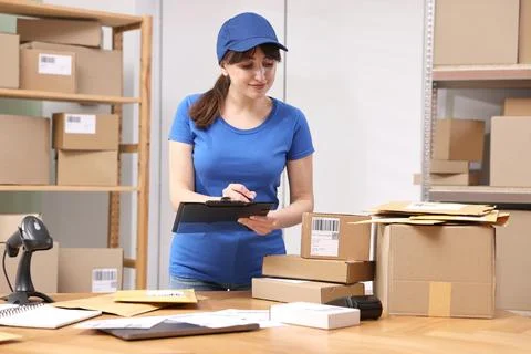 Parcel packing. Post office worker with clipboard at wooden table indoors Foto stock