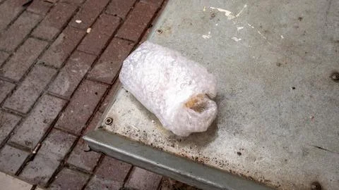 Parcel wrapped in bubble wrap on dirty metal surface next to brick pavement Stock Photos