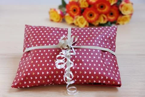 Parcel wrapped in heart patterned paper and flowers on wooden table, closeup Stock Photos