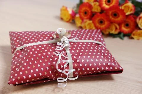 Parcel wrapped in heart patterned paper and beautiful flowers on wooden tab.. 스톡 사진